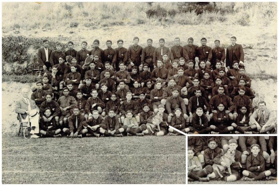 Class photo of Te Auto College, New Zealand, in 1910, featuring a small dog being held by a boy in the front row.