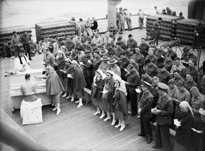 Black and white photo of people aboard a Hospital Ship, attending a service. There is a man playing the piano on the left. 